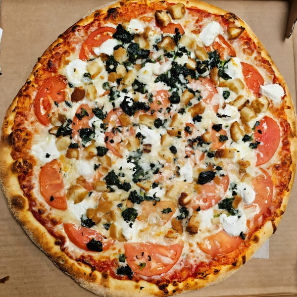 Casa Bianca Pizza with tomatoes, spinach, chicken, and dollops of ricotta cheese in a box.