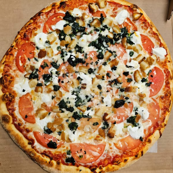 Casa Bianca Pizza with tomatoes, spinach, chicken, and ricotta cheese in a pizza box.