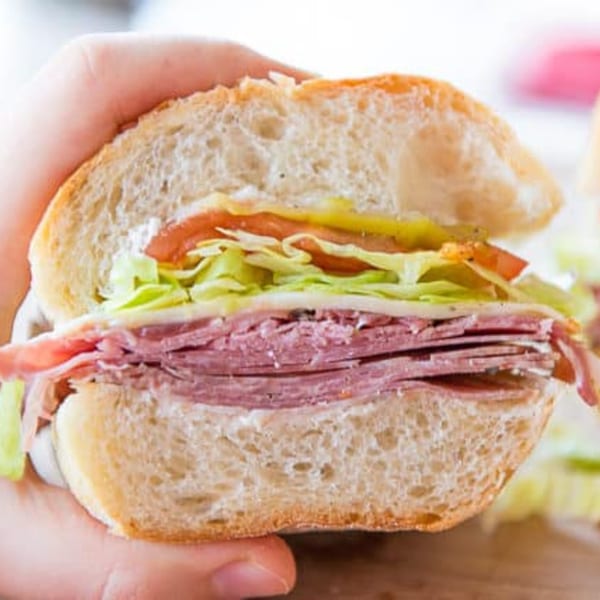Hand holding a cross-section of a sub sandwich with meat, cheese, lettuce, and tomato.