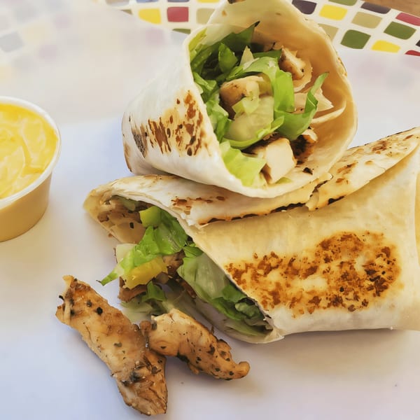 Two grilled chicken and lettuce wraps with a side of dipping sauce on a white surface.