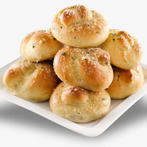 A white plate piled high with golden-brown Casa Bianca Pizza garlic knots, sprinkled with cheese and herbs.