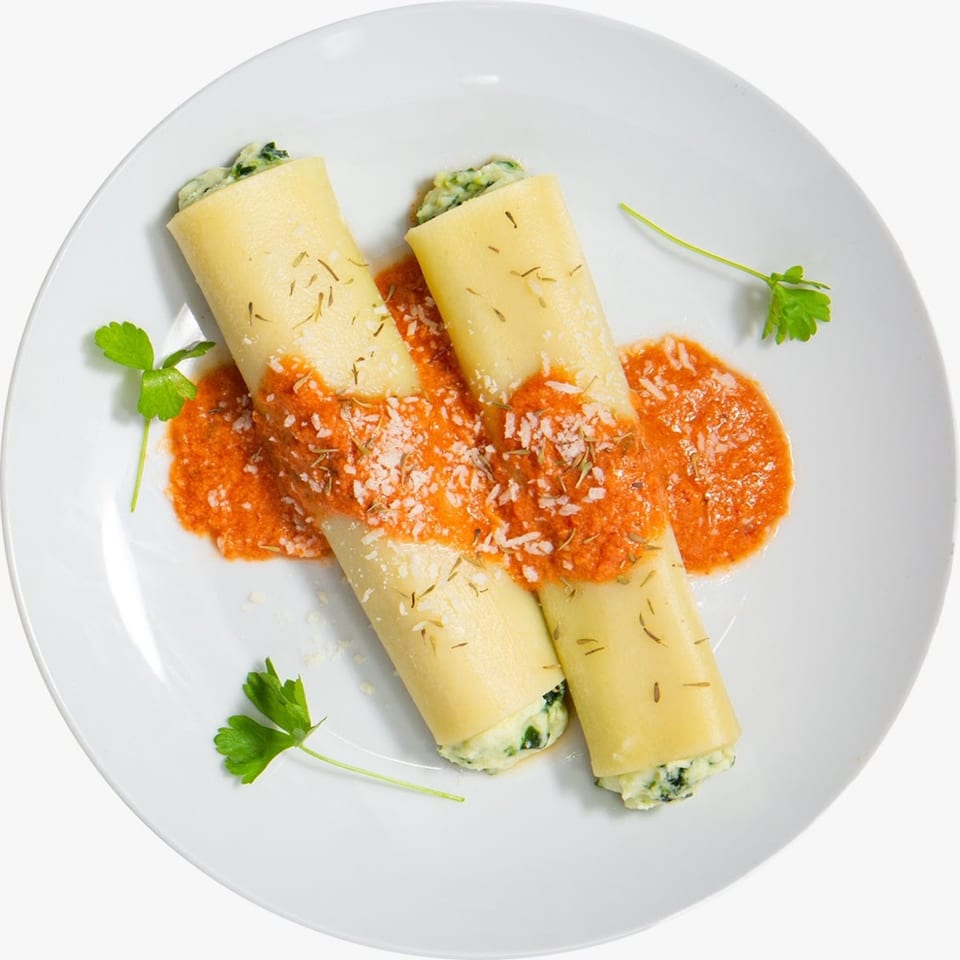 Two spinach and ricotta cannelloni topped with tomato sauce, parmesan, and herbs on a white plate.