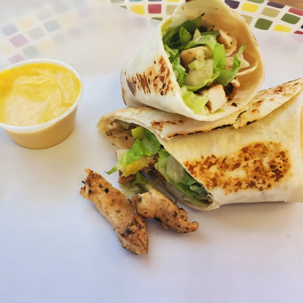 Two chicken wraps filled with lettuce and chicken, alongside a cup of dipping sauce.