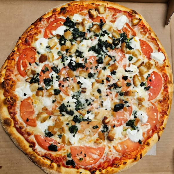 Casa Bianca Pizza with tomatoes, spinach, chicken, and ricotta cheese in a delivery box.