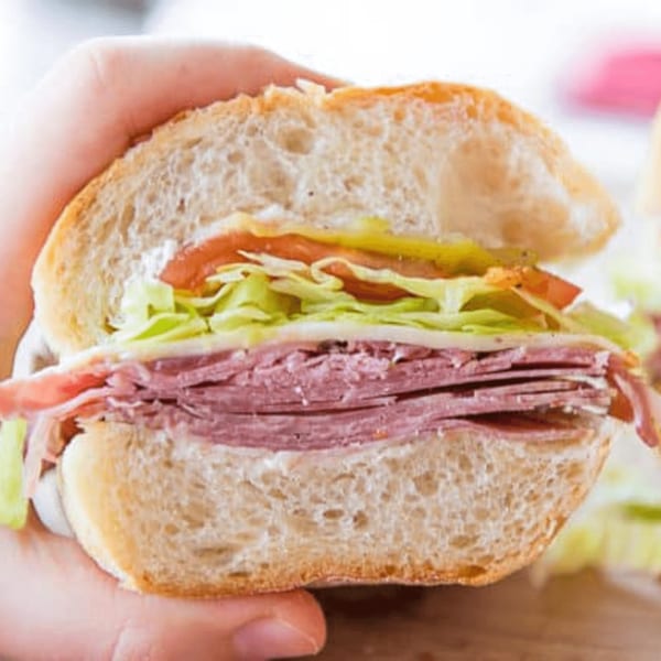 A hand holds a sliced Casa Bianca sub sandwich filled with deli meat, lettuce, tomato, and cheese.